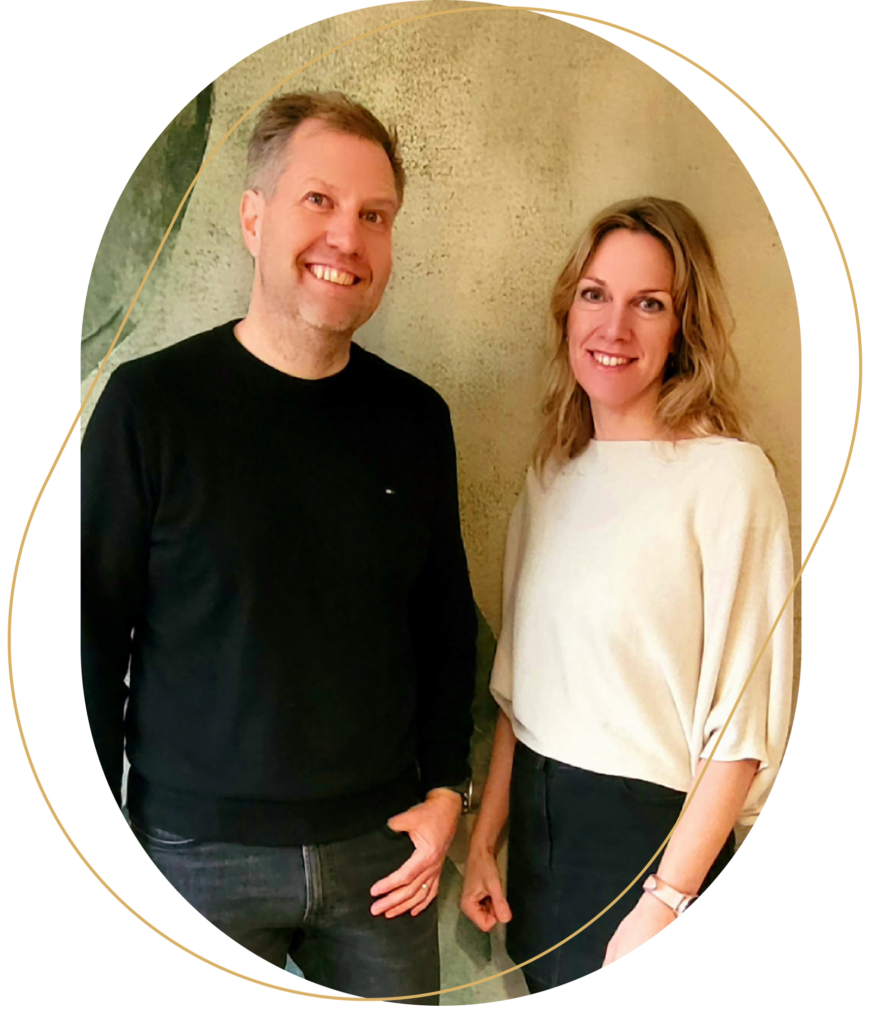 Zwei Beraterinnen und Berater stehen nebeneinander und lächeln in einem hellen Raum mit Holzoptik.